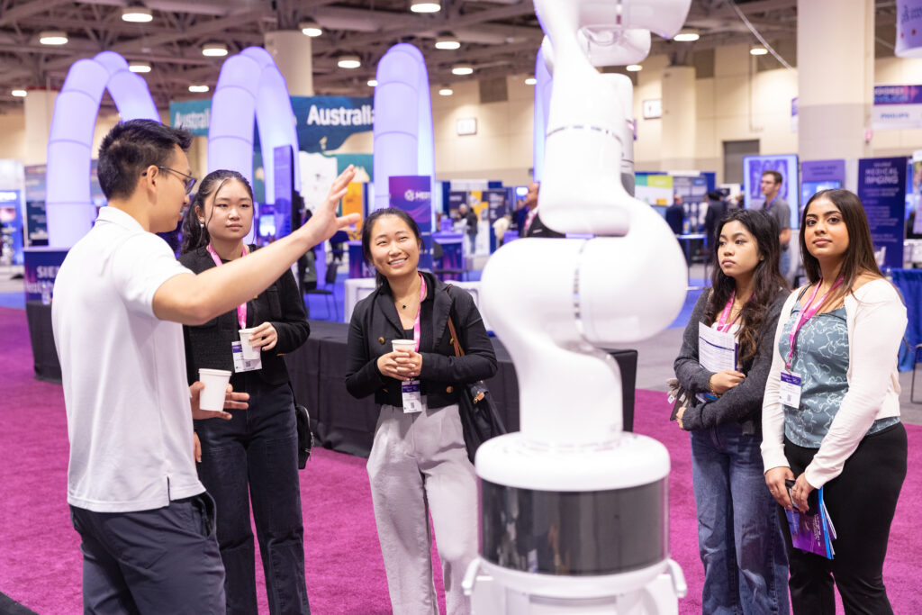 group of people standing around a white robotic medtech device at the medtech conference